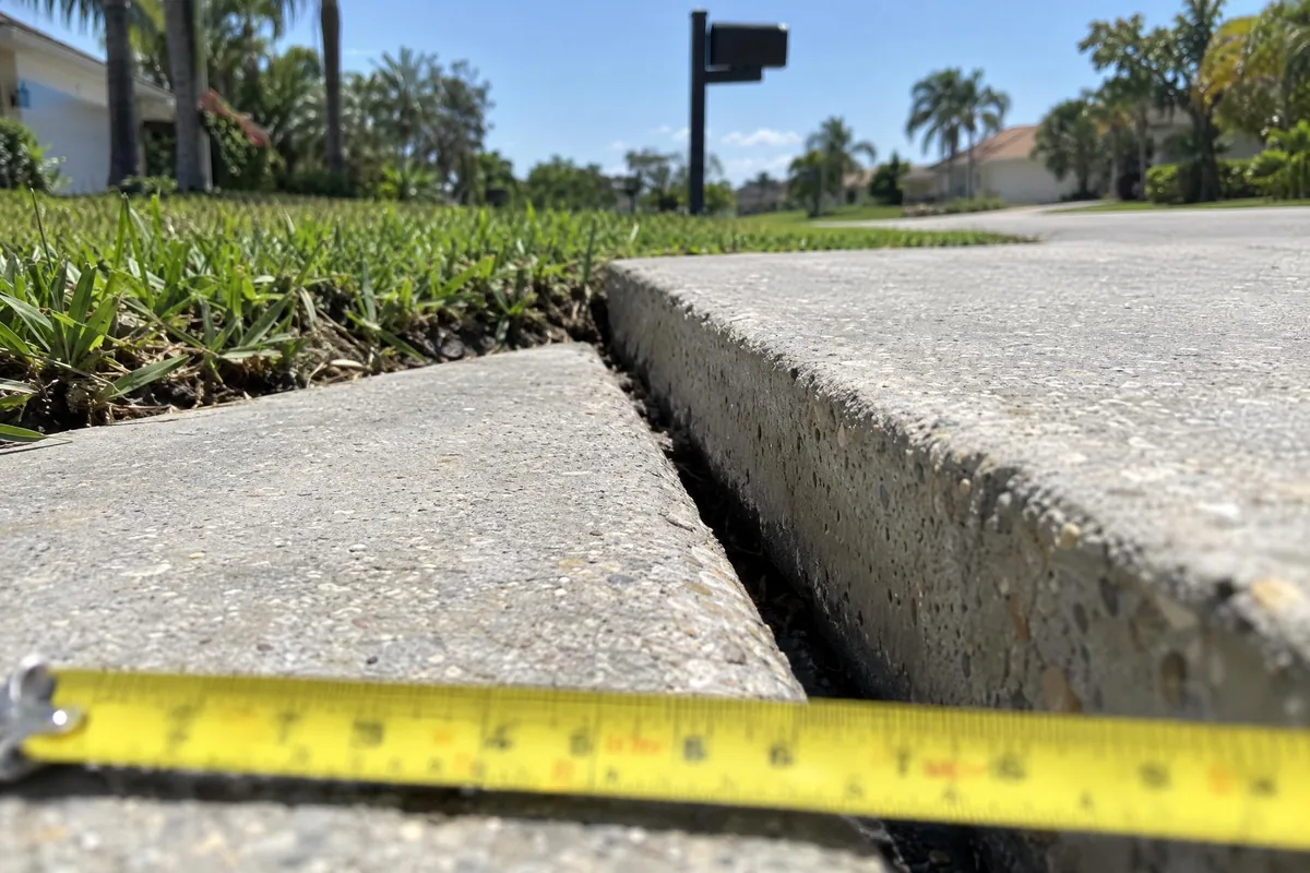 A driveway slab sitting higher than its neighbor with a tape measure across the gap